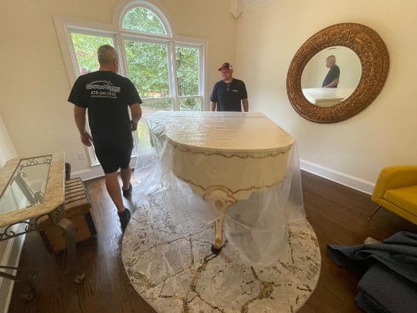 Professional movers transporting a piano during long-distance move in a bright living room.