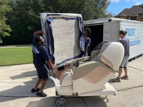 Moving chair being carefully loaded onto a moving truck by professional movers.